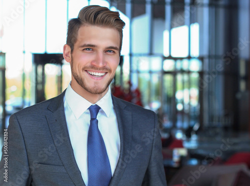 Portrait of happy young businessman standing in hotel lobby. © ty