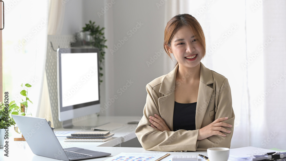 Pretty female employee sitting in modern office and smiling confidently to camera. Pretty female employee sitting in modern office and smiling confidently to camera.