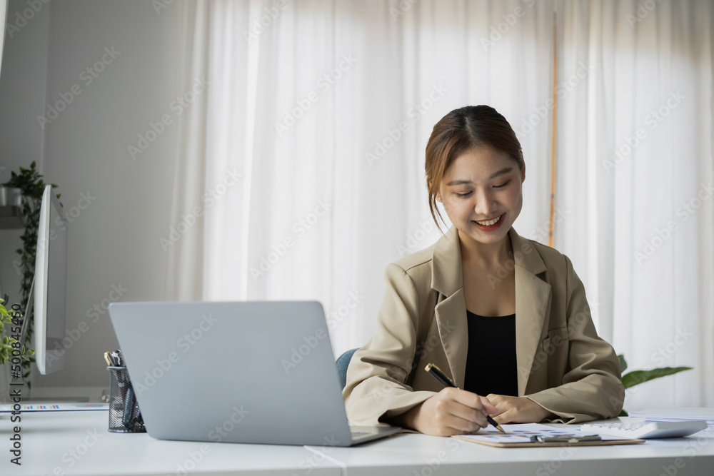 Beautiful female employee using laptop computer and making important notes on notebook. Beautiful female employee using laptop computer and making important notes on notebook.