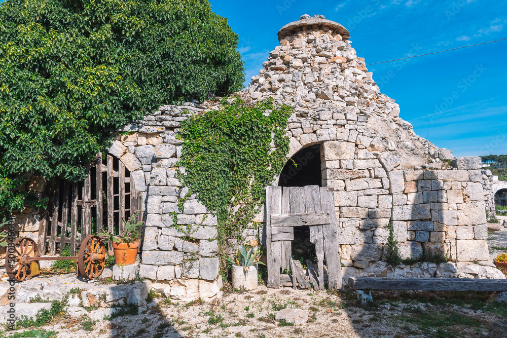 Ruins of abandoned Trulli or Trullo house, traditional Apulian dry stone hut with a conical roof, old dry stone walls and rusty wheel of an old wagon in Puglia, Italy