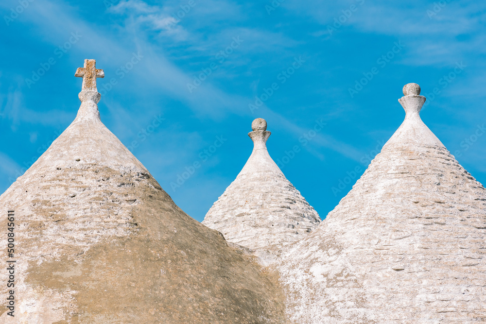 White roof of beautiful Trulli or Trullo house, traditional Apulian dry stone hut with a conical roof and old dry stone walls in Puglia, Italy, with blue sky and cross