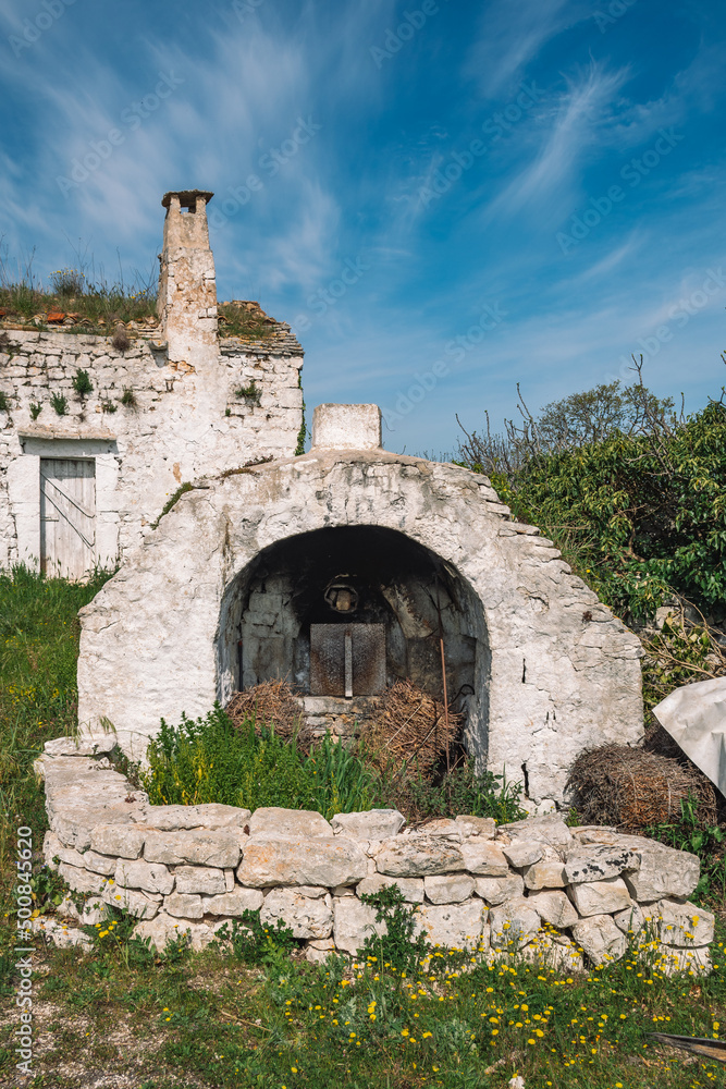 Beautiful white traditional old stone outdoor oven or fireplace in the countryside in Puglia region, Italy with white old farm, finca or cottage, vertical