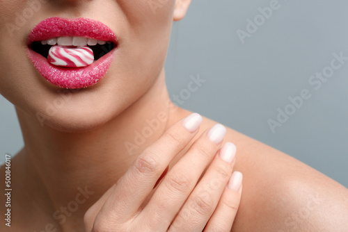 Woman with lips covered in sugar eating candy on light grey background  closeup. Space for text