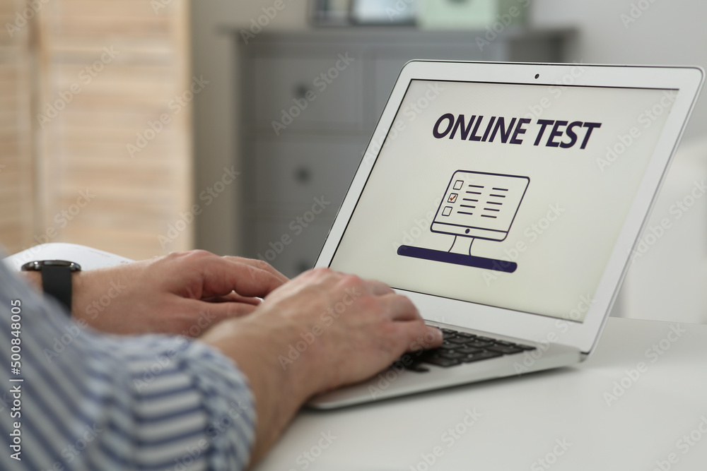 Man taking online test on laptop at desk indoors, closeup Man taking online test on laptop at desk indoors, closeup