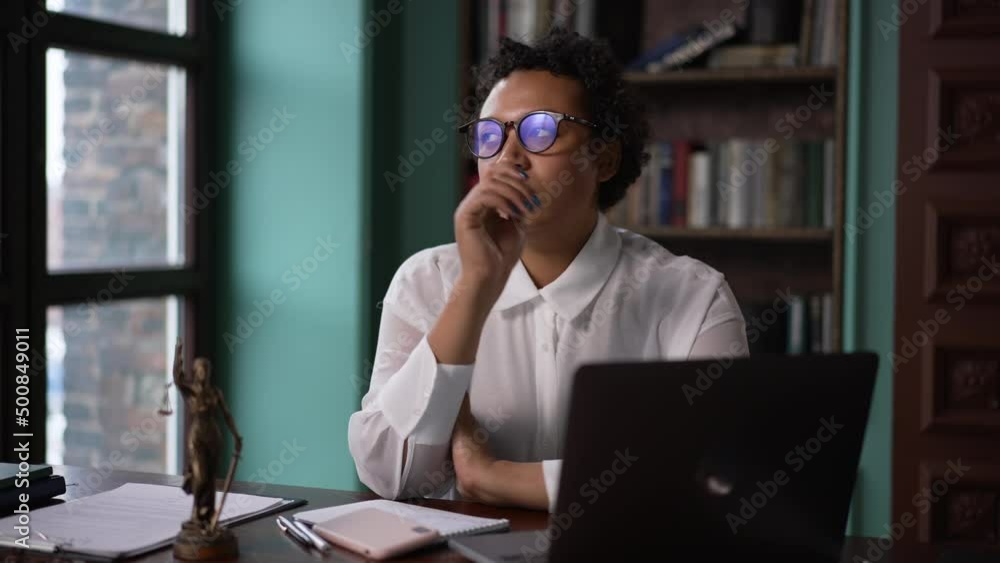 Young female professional lawyer working with laptop and resting, sitting at table in company spbas. 4k Portrait of beautiful american african woman looks at computer screen and types then rests or Young female professional lawyer working with laptop and resting, sitting at table in company spbas. 4k Portrait of beautiful american african woman looks at computer screen and types then rests or