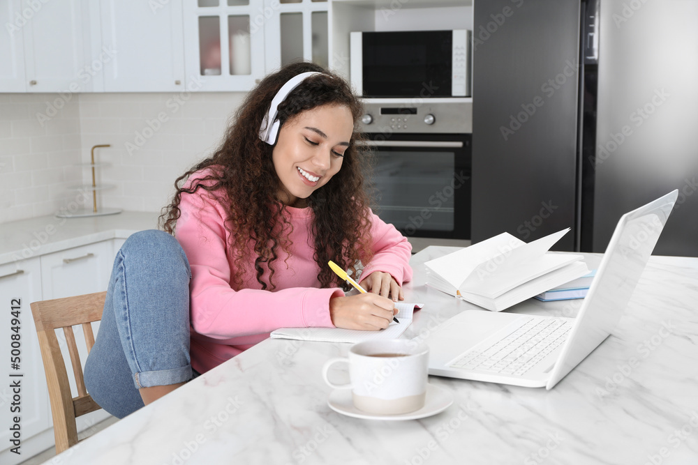 African American woman with modern laptop and headphones studying in kitchen. Distance learning African American woman with modern laptop and headphones studying in kitchen. Distance learning