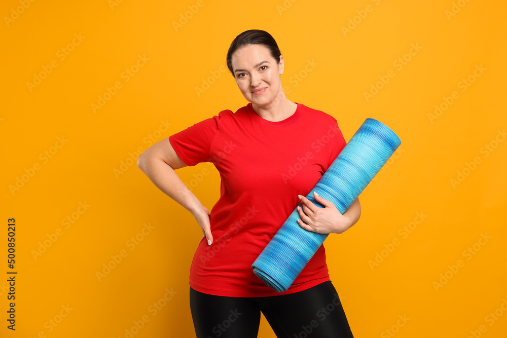 Happy overweight woman with yoga mat on orange background Happy overweight woman with yoga mat on orange background
