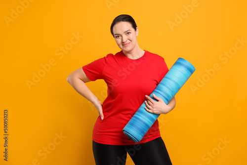 Happy overweight woman with yoga mat on orange background