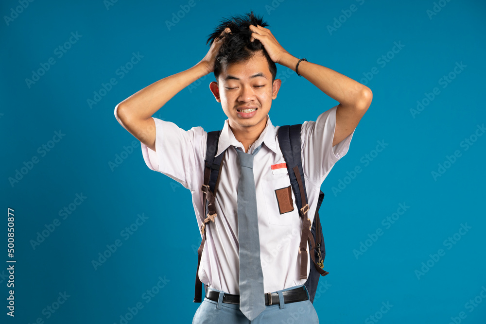 Dizzy Indonesian high school student holding his head isolated on blue background Dizzy Indonesian high school student holding his head isolated on blue background