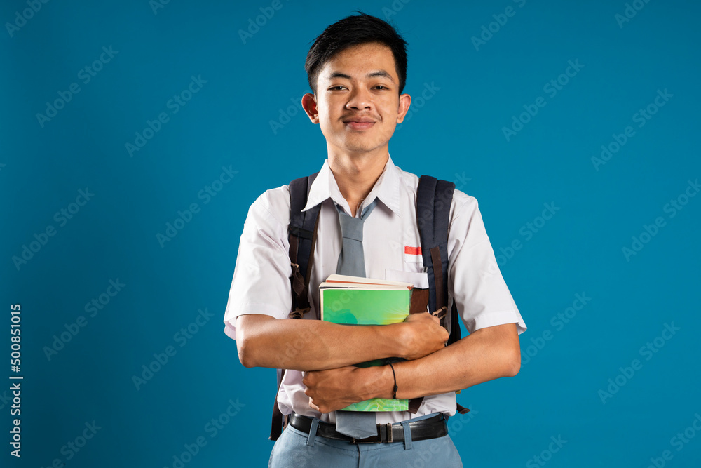 Back to school. Portrait of a Indonesian high school student smiling at the camera holding a book on a blue background. Back to school. Portrait of a Indonesian high school student smiling at the camera holding a book on a blue background.