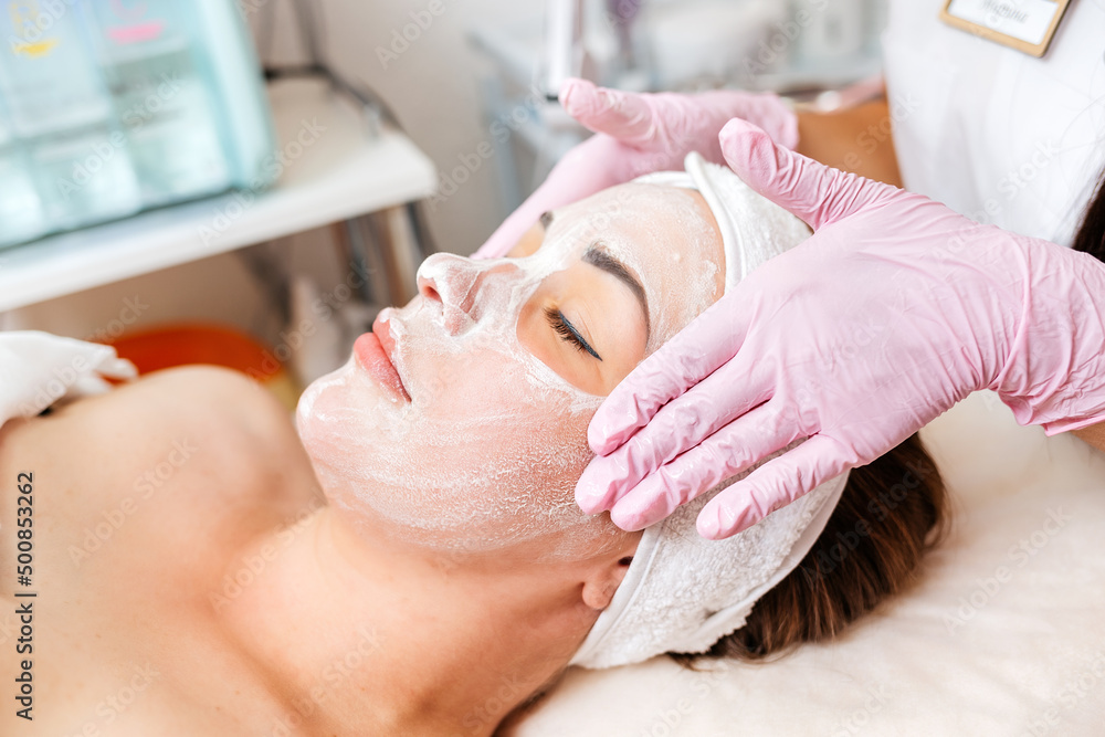 Cosmetologist's hands at protective gloves massages client's face with cosmetics mask. Concept of professional cosmetology Cosmetologist's hands at protective gloves massages client's face with cosmetics mask. Concept of professional cosmetology