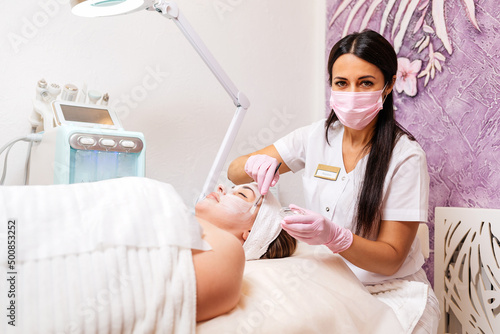 New normal. Professional female cosmetologist in a protective mask and gloves, applies the mask to the client's face. The concept of professional cosmetology service