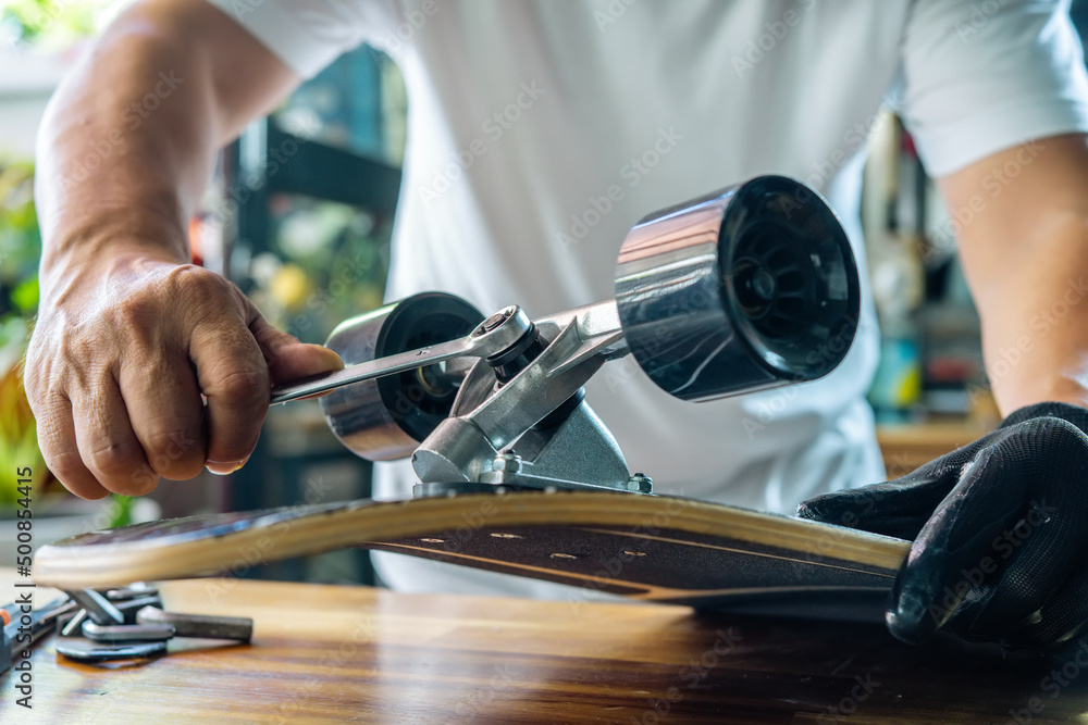 man use the socket tool to remove the nuts on skateboard and adjusts suspension in workshop, Skateboard maintenance and repair concept. Selective focus
