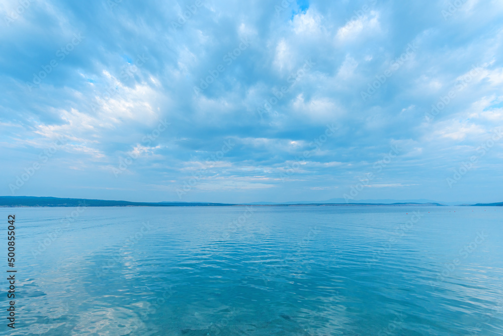 Tranquil sea water surface with rippled reflection of the clouds and sky