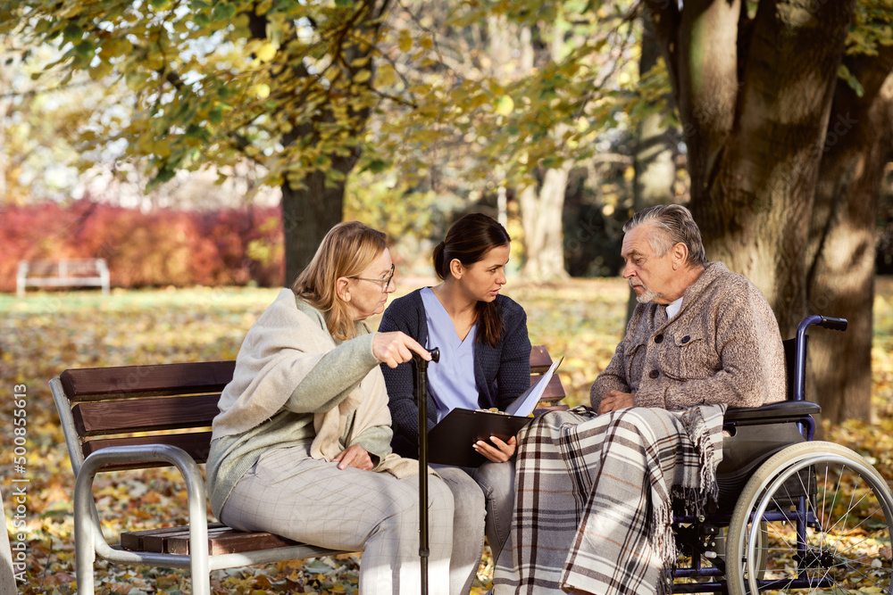 Caretaker discussing documents with disabled man and senior woman at park Caretaker discussing documents with disabled man and senior woman at park