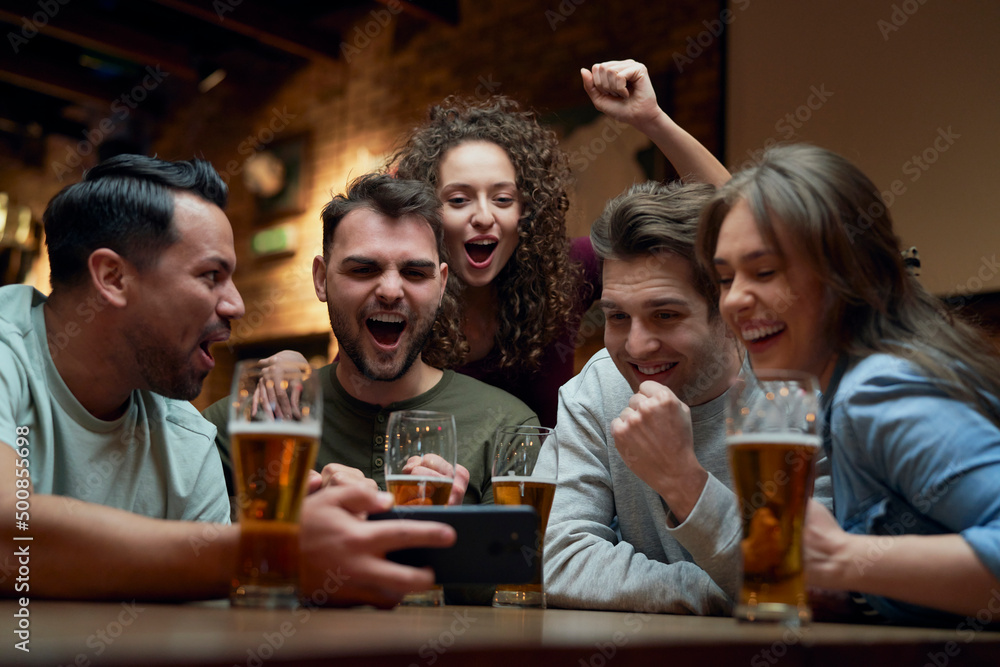 Group of cheerful soccer fans having beer and watching a match on smartphone in a pub Group of cheerful soccer fans having beer and watching a match on smartphone in a pub
