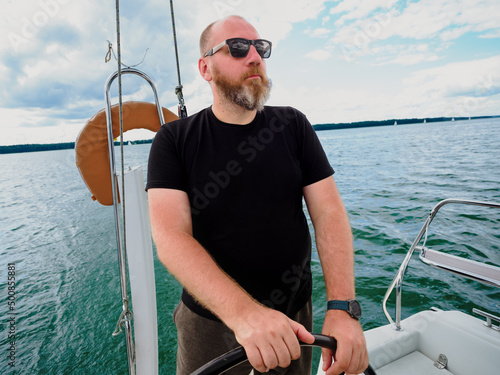 adult bearded man steering wheel a sailing yacht