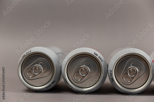 Three full tin cans lie against the gray background. Cylindrical silver individual beverage containers
