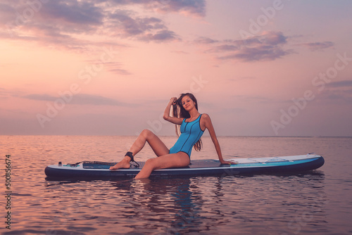 Canvas Print A young smiling sporty woman poses sitting on a sup board
