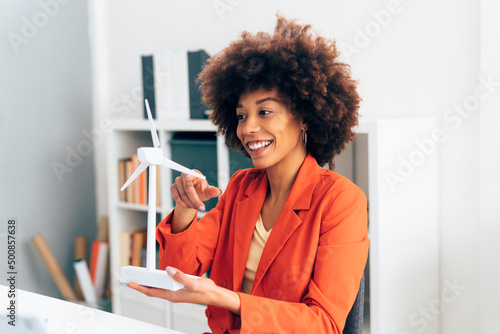 Smiling businesswoman with windmill model sitting in office photo