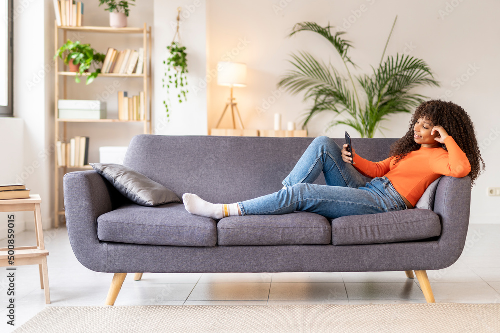 Young woman using smart phone sitting on sofa in living room Young woman using smart phone sitting on sofa in living room