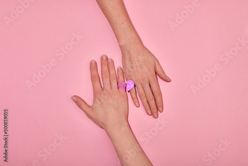 Top view hands of anonymous hands forming heart with similar rings on fingers on pink background in light studio