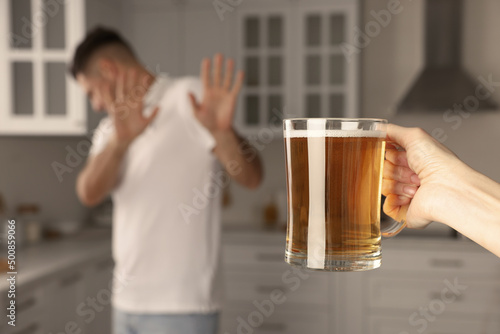 Man refusing to drink beer in kitchen, closeup. Alcohol addiction treatment