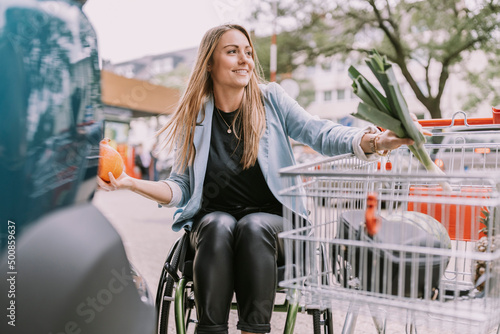 Smiling woman with groceries sitting in wheelchair by shopping cart photo