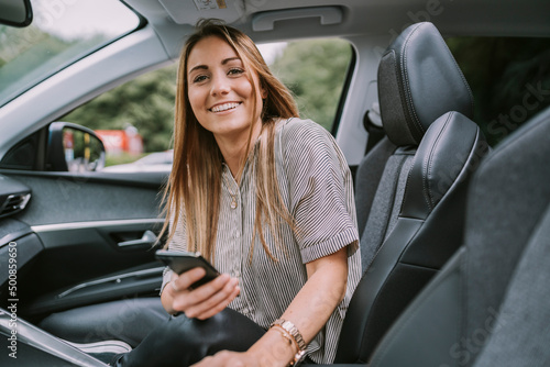 Happy blond woman with smart phone sitting on front passenger seat in car photo