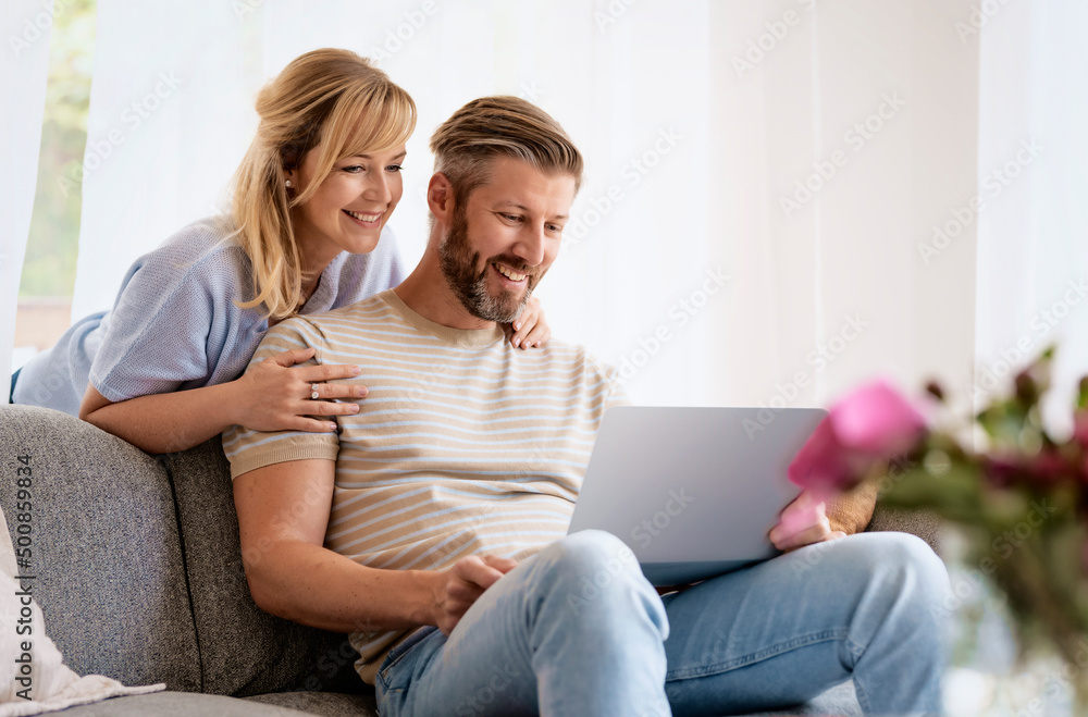 Happy couple sitting on couch at home and using laptop