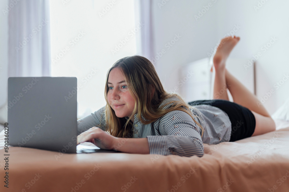 Smiling woman using laptop lying on bed at home Smiling woman using laptop lying on bed at home