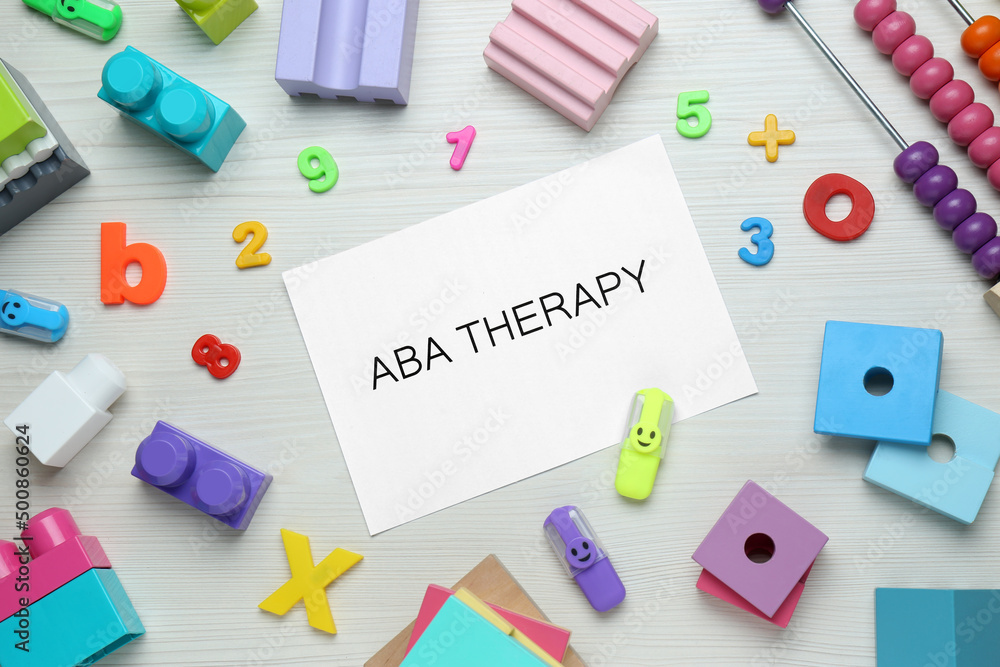 Flat lay composition with phrase ABA Therapy and colorful toys on white wooden table Flat lay composition with phrase ABA Therapy and colorful toys on white wooden table