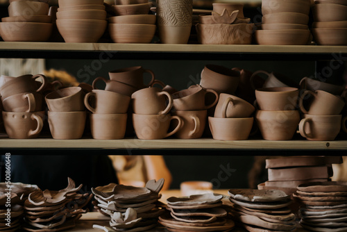 Handmade ceramic bowls with cups and plates on shelf in workshop photo