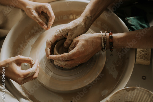 Hands of Instructor teaching young man molding bowl on potter's wheel in workshop photo