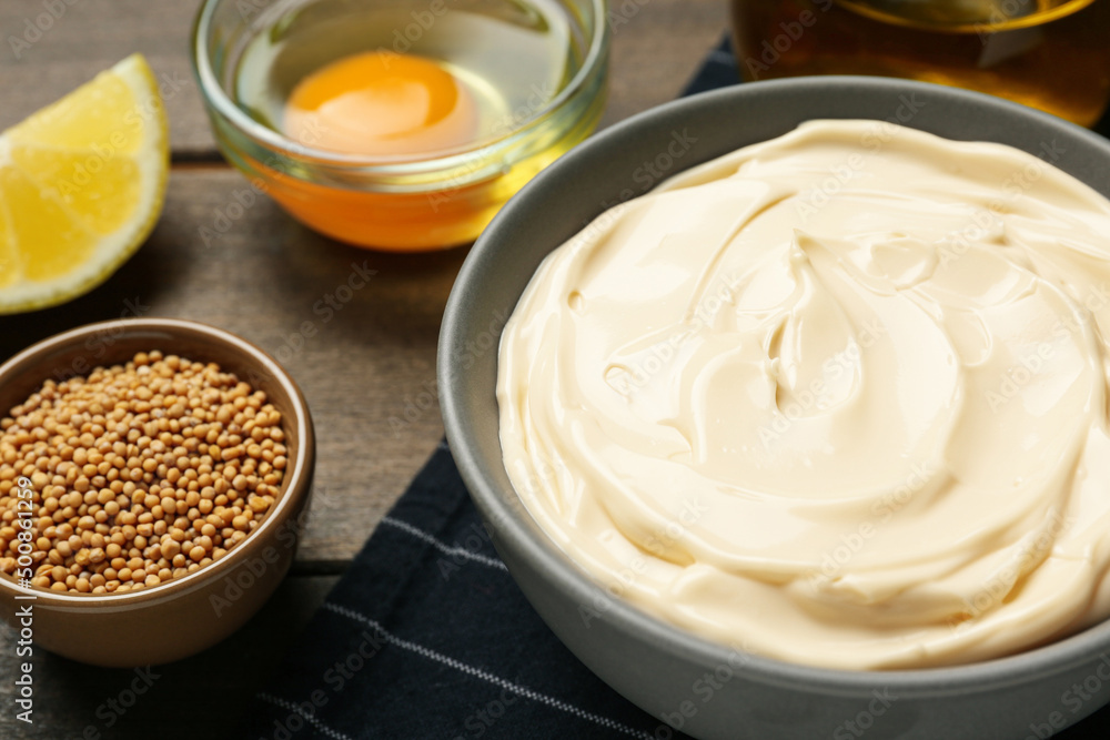 Bowl with fresh mayonnaise and ingredients on wooden table, closeup Bowl with fresh mayonnaise and ingredients on wooden table, closeup