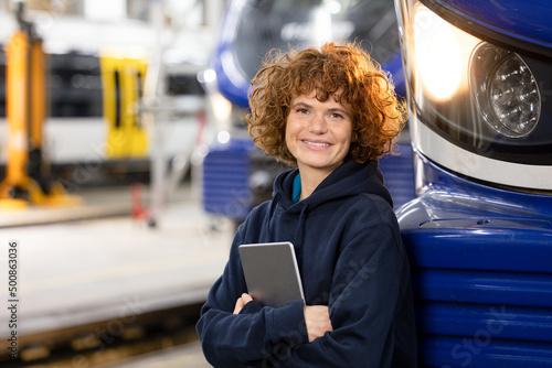 Smiling engineer holding tablet PC leaning on monorail in factory photo