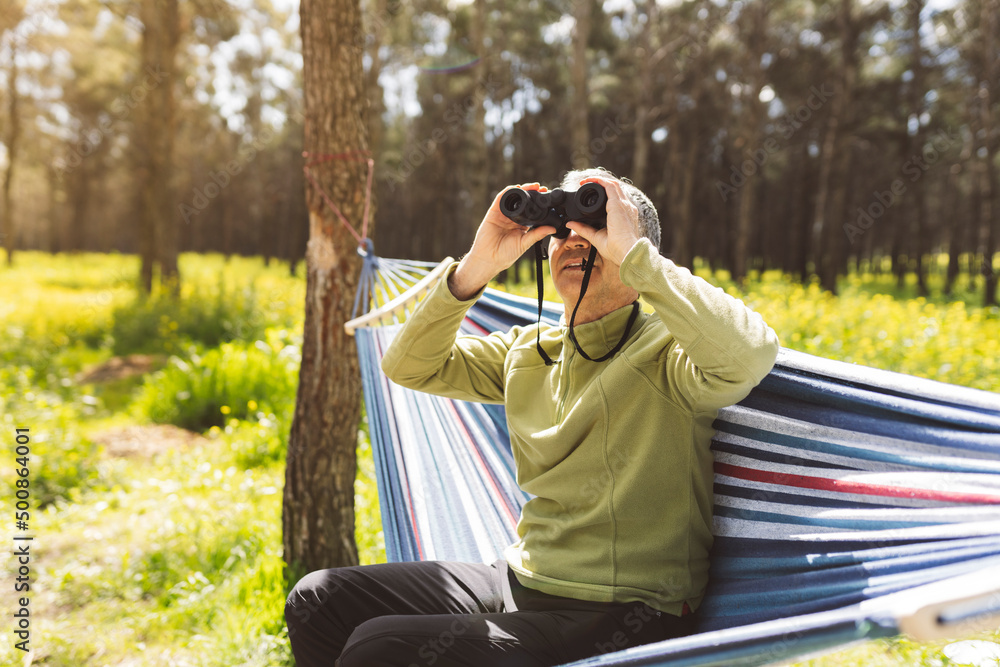 Man looking through binoculars sitting in hammock on sunny day Man looking through binoculars sitting in hammock on sunny day