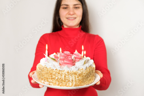 A brunette woman in red clothes holds a large white cake with candles, makes a wish