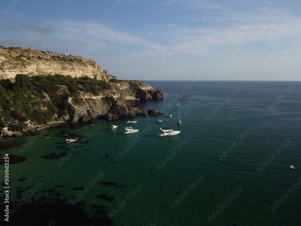 Aerial panoramic view of seascape with crystal clear azure sea and rocky shores. Yachts in a beautiful lagoon on backdrop of rocks. The concept of an ideal destination for summer travel and vacation.