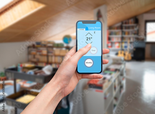 Hand holding a mobile phone showing an home automation app to manage smart technology in a modern house
