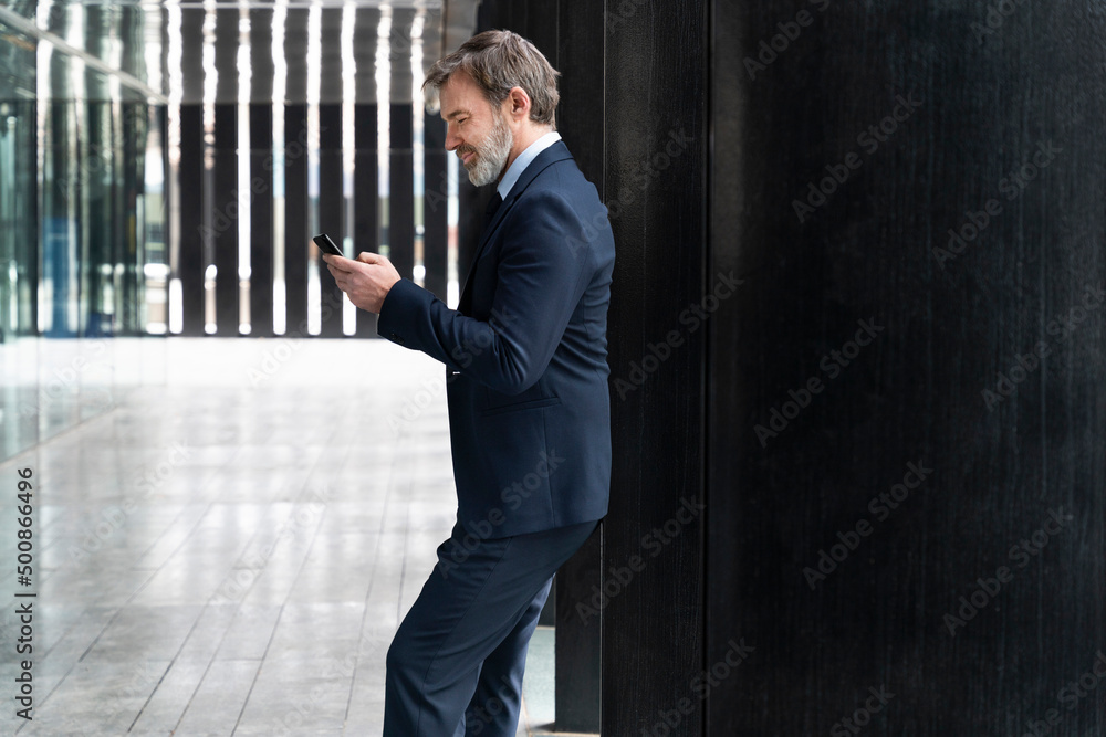 Businessman using smart phone leaning on black column Businessman using smart phone leaning on black column