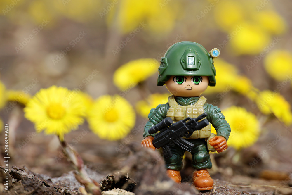 Toy soldier on background of spring flowers of coltsfoot. Concept of military forces, modern war Toy soldier on background of spring flowers of coltsfoot. Concept of military forces, modern war