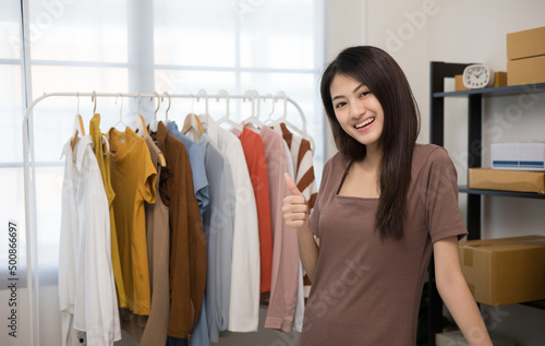 Happy Young beautiful asian woman business owner at fashion store check stock on rails clothing standing and smile. Asian female entrepreneur working in clothes shop.