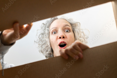 Surprised woman opening cardboard box at home photo