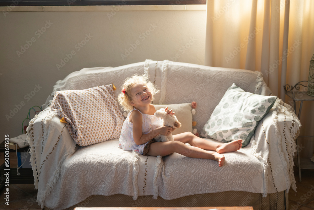 Happy girl holding toy sitting on sofa at home Happy girl holding toy sitting on sofa at home
