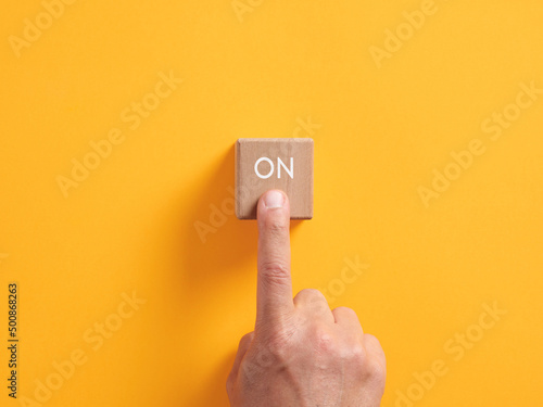 Male hand presses on a wooden cube with the word on. Power on push button business startup activation photo