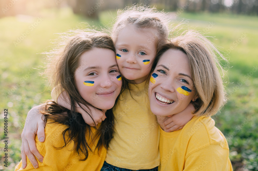 Fototapeta premium Portrait of Ukrainian family. Mom with two little daughters hugging and smiling in nature on sunny day.