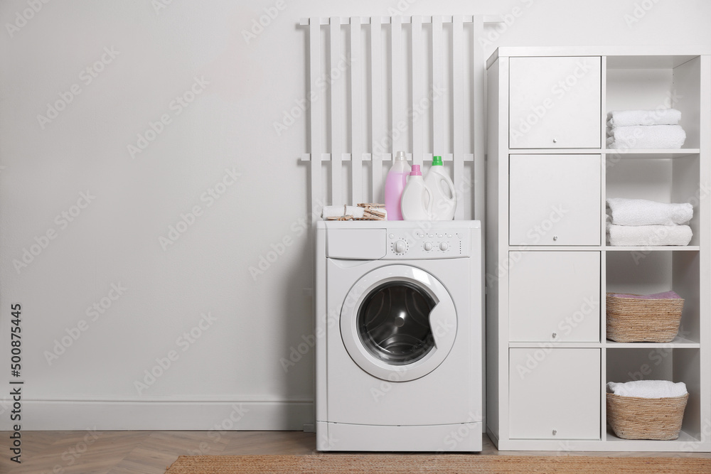 Laundry room interior with modern washing machine and shelving unit near white wall Laundry room interior with modern washing machine and shelving unit near white wall