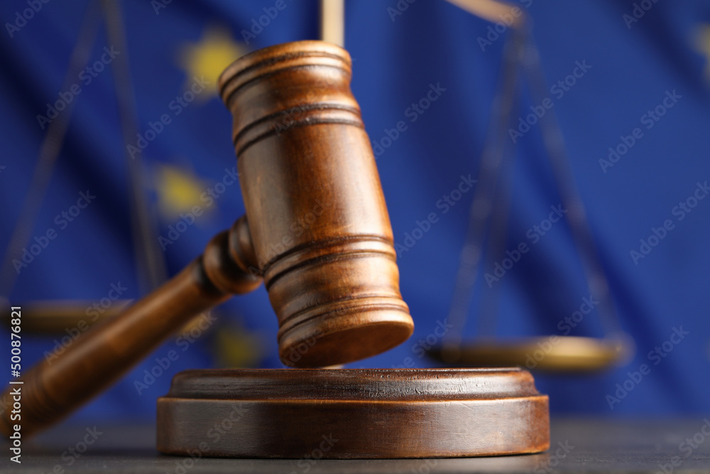 Wooden judge's gavel and Scales of justice on grey table against European Union flag, closeup Wooden judge's gavel and Scales of justice on grey table against European Union flag, closeup