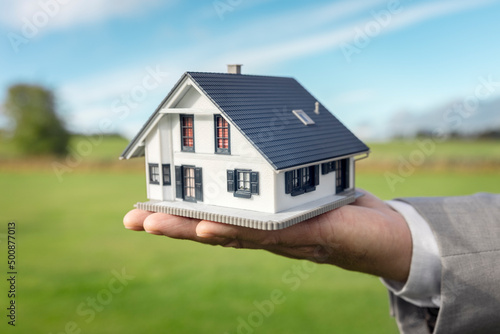 Holding a model detatched house in empty field background concept for construction and real estate